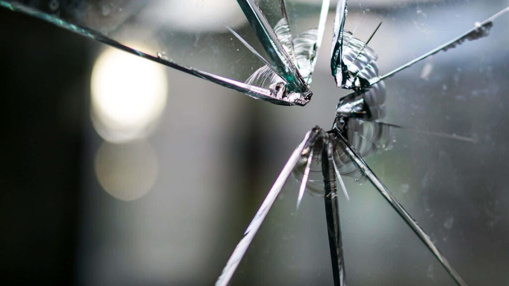 Close-up shattered glass explosion wallpaper with sharp fragments dramatic cracks metallic tones