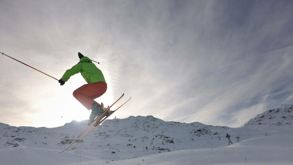 Dynamic Ski Jump Wallpaper: Skier Mid-Air with Snowy Mountains