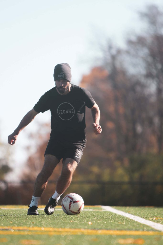Bearded soccer player in black Techne beanie and shirt dribbles on turf with autumn background Wallpaper