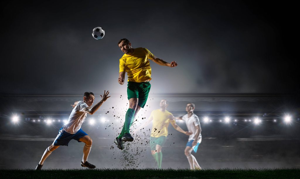 Dynamic soccer players in yellow and white jerseys competing for a header under stadium lights Wallpaper