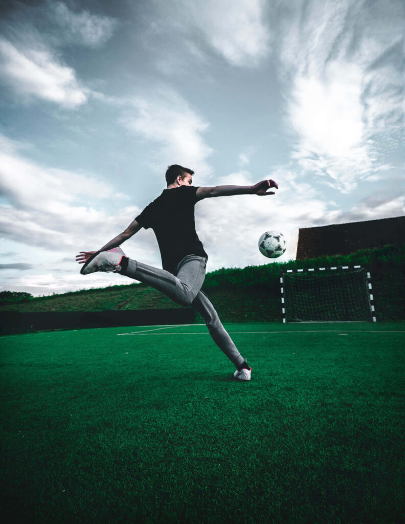 Dynamic Soccer Player Kicking Ball: Scenic Green Field Wallpaper
