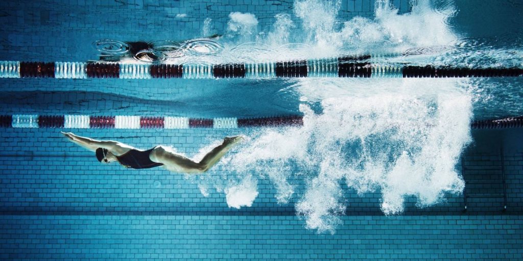 Female swimmer diving underwater in pool with bubbles and blue tiled background wallpaper