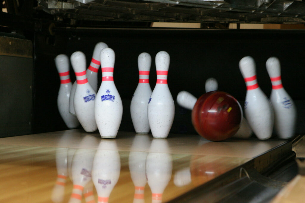 High-resolution action shot of red bowling ball striking white pins on glossy wooden lane wallpaper