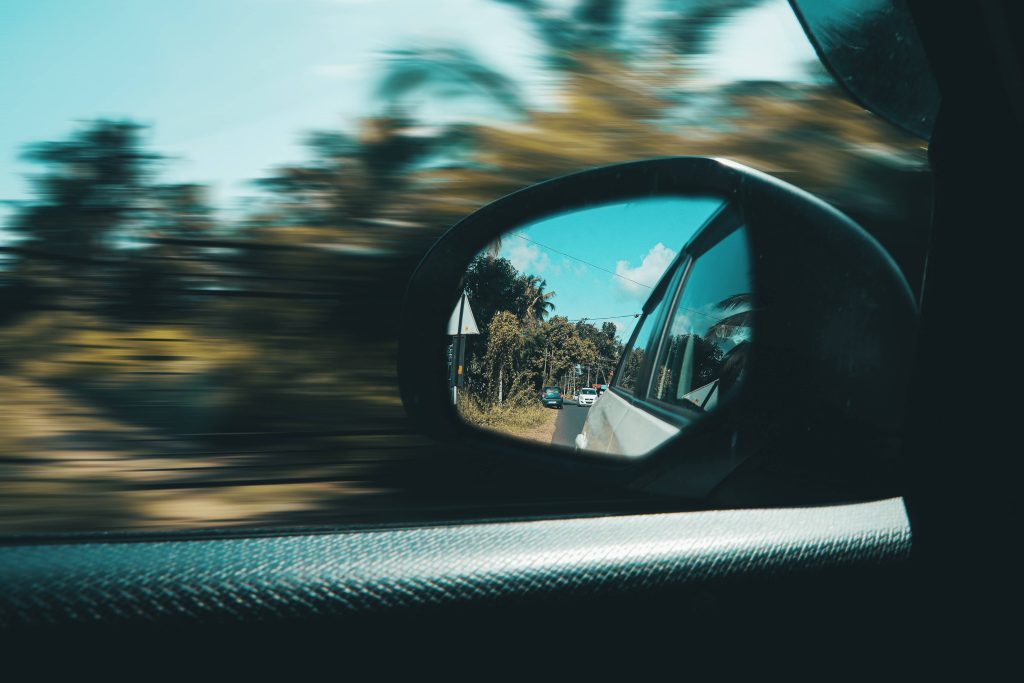 Dynamic car side mirror view showing blurred landscape and sharp reflection of cars trees sky Wallpaper
