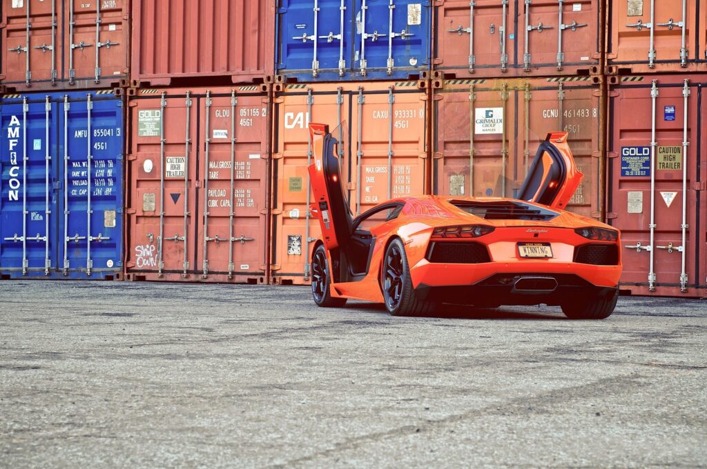 Orange Lamborghini Aventador in Front of Colorful Shipping Containers Wallpaper