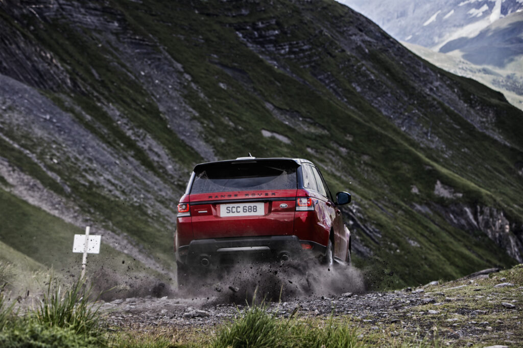 Red Range Rover Sport Off-Roading on Gravel with Mountain Background Wallpaper