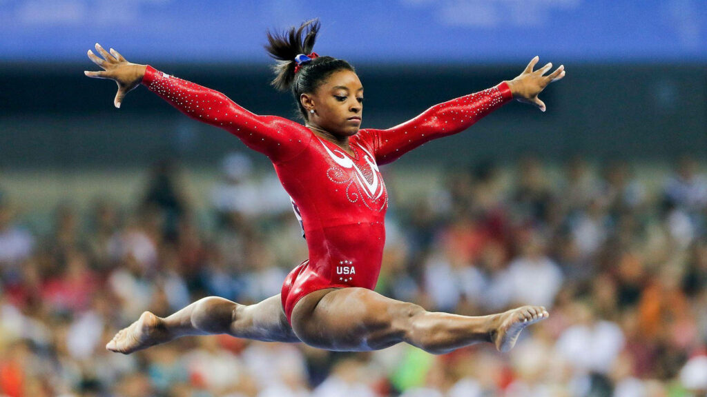 Simone Biles Split Jump: Dynamic Gymnastics Wallpaper Background