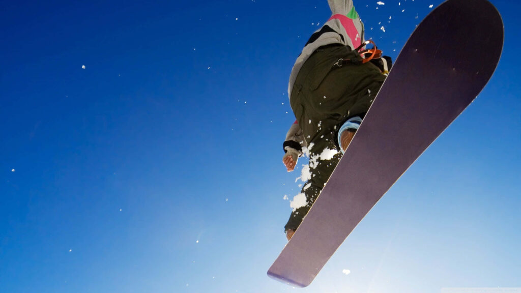 Thrilling Snowboarder Mid-Air Wallpaper Against Blue Sky Background