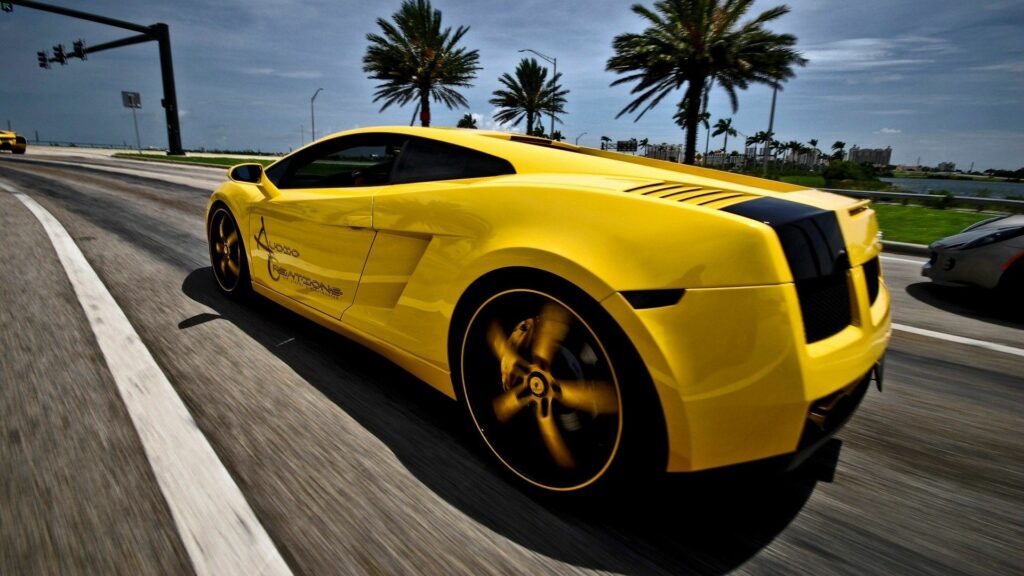 Vibrant Yellow Lamborghini Speeding Through Scenic Palm Tree Road Wallpaper