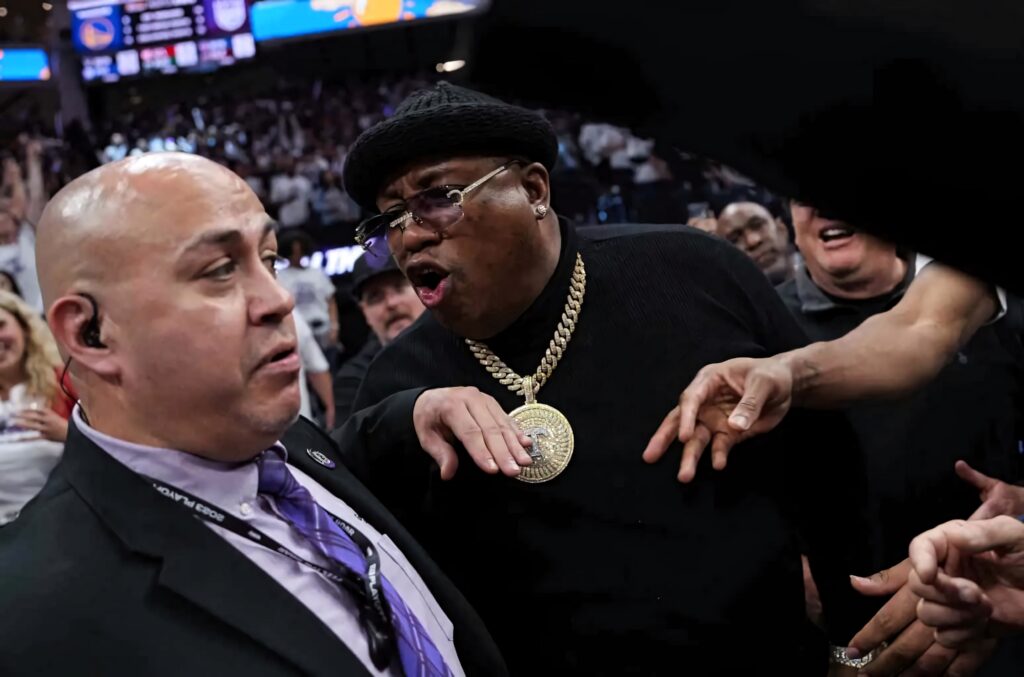 E-40 animatedly confronts arena security in a crowded vibrant sports arena with energy and tension Wallpaper