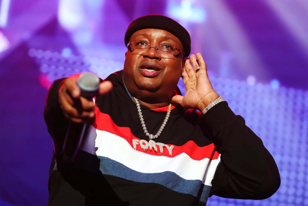 E-40 performing live on stage with microphone vibrant lighting bold striped sweatshirt dynamic energy Wallpaper