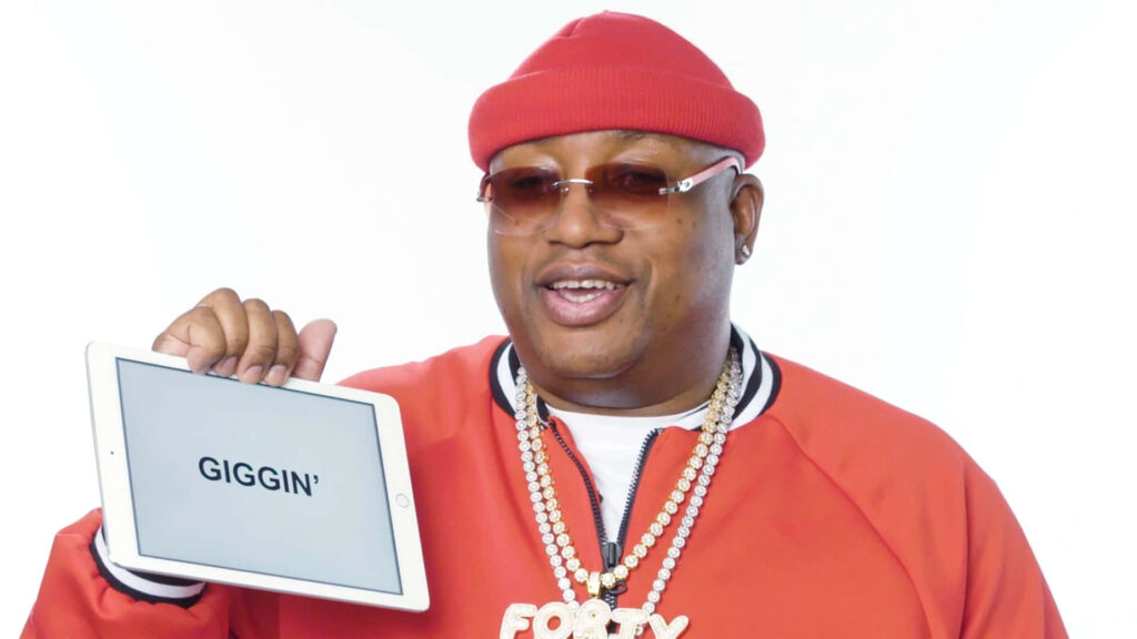 E-40 in vibrant red outfit with gold chains holding Giggin tablet on white background hip-hop style Wallpaper