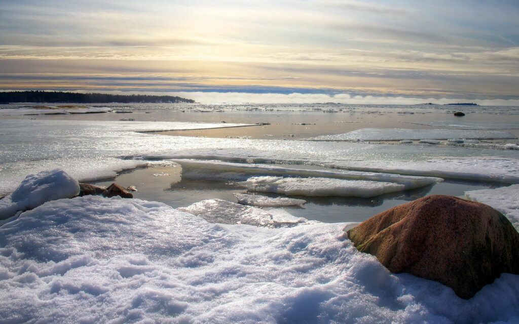 Early spring shoreline with melting ice snow soft sunlight reflections peaceful landscape wallpaper