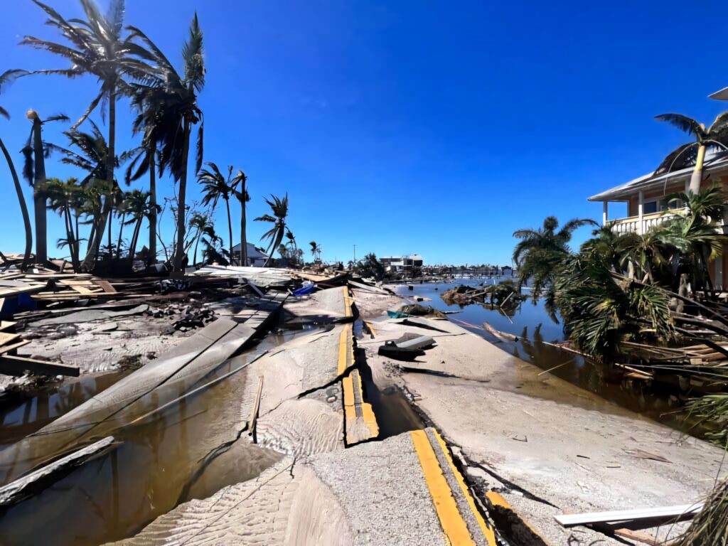 Cracked sunken road with leaning palm trees and damaged buildings after earthquake under blue sky Wallpaper