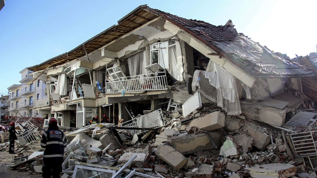Severely damaged residential building after earthquake with emergency responders amid debris in daylight Wallpaper