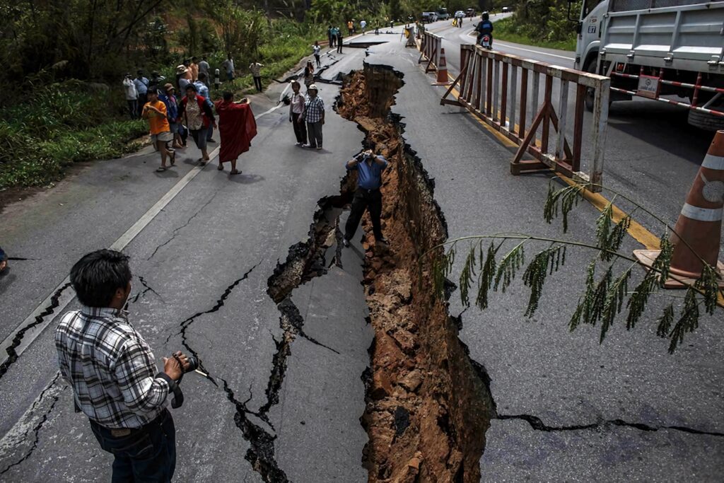 Earthquake aftermath with massive road fissure groups of people observing damage lush greenery background Wallpaper