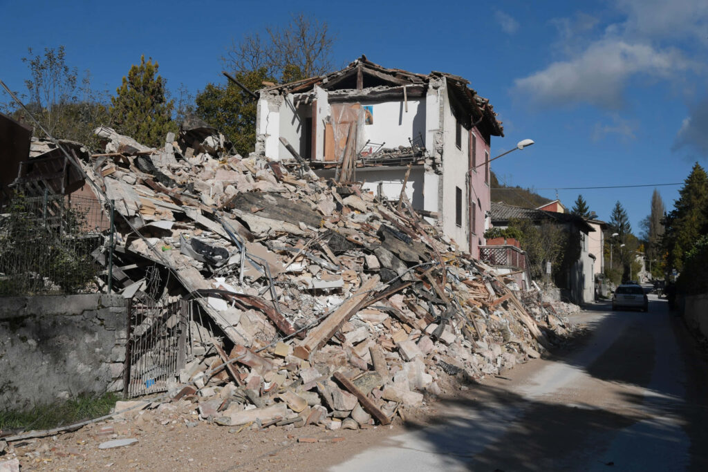Partially collapsed house and rubble after earthquake under clear blue sky wallpaper background