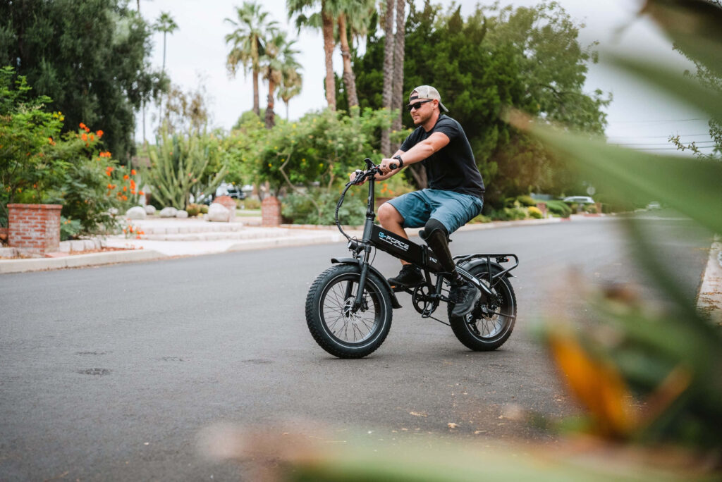 Man riding electric bike on sunny suburban street with lush greenery and palm trees background Wallpaper