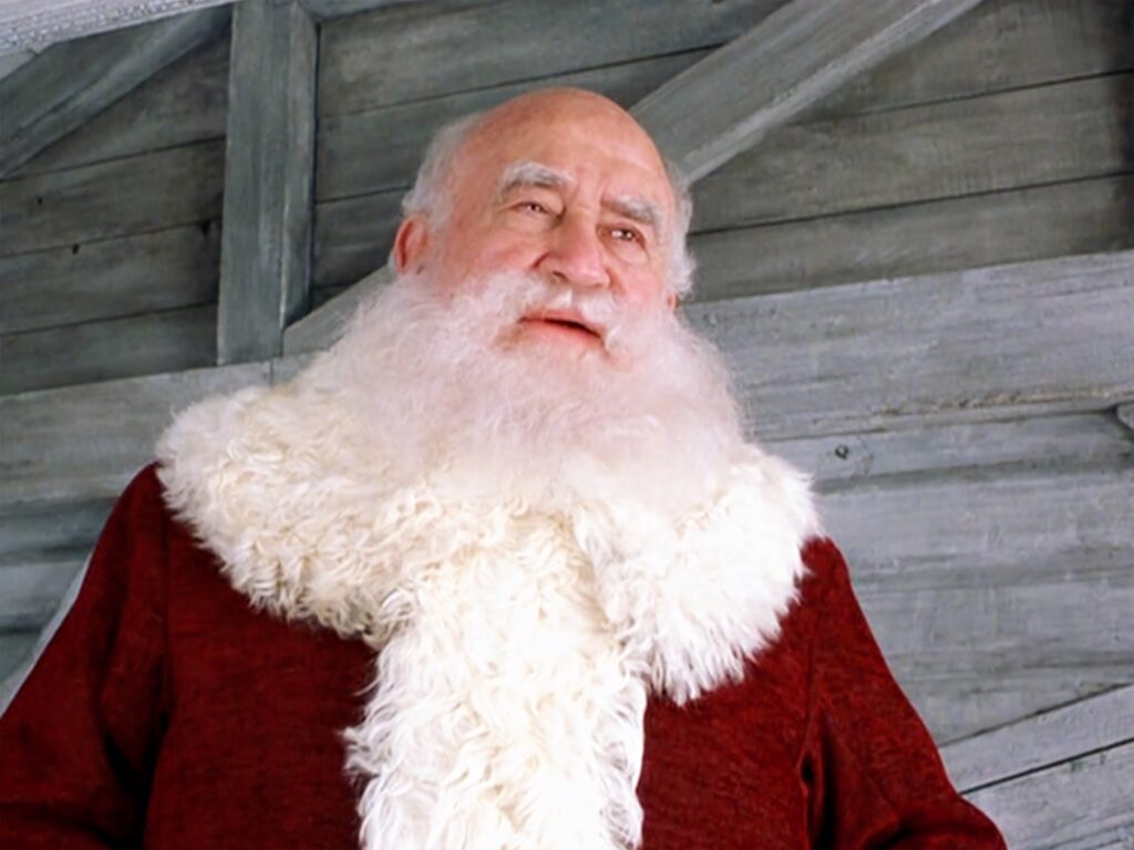 Ed Asner as Santa Claus in red coat and white beard with rustic wooden festive background wallpaper
