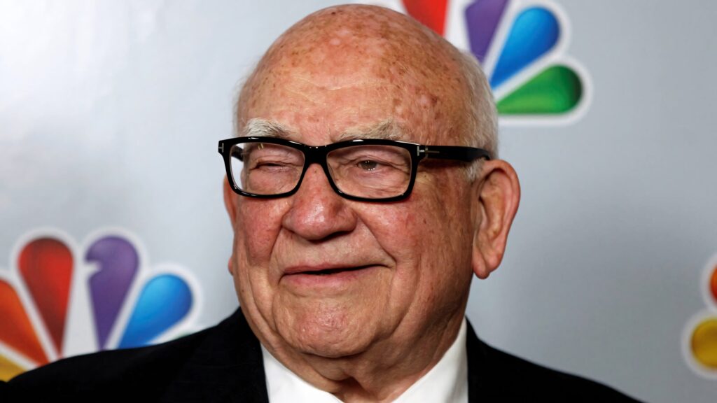 Ed Asner smiling warmly in front of colorful NBC logo classic TV legend portrait wallpaper