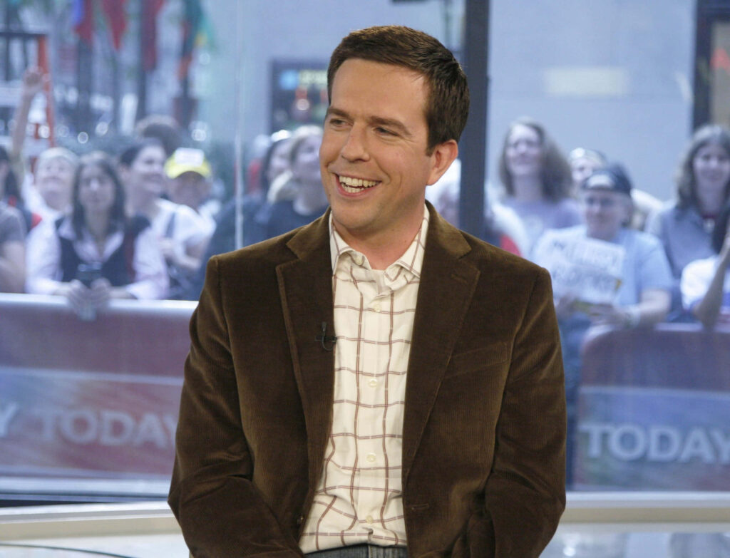 Ed Helms in brown velvet blazer smiling in studio with lively crowd during TV interview wallpaper