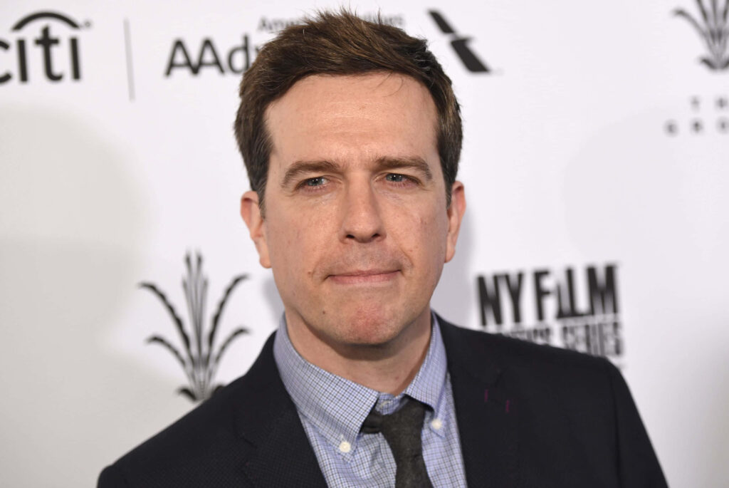 Ed Helms in dark suit and checkered shirt posing in high resolution wallpaper with event logos background