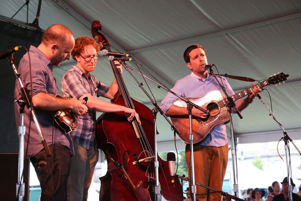 Ed Helms performing live acoustic music with guitar mandolin and upright bass under event tent Wallpaper