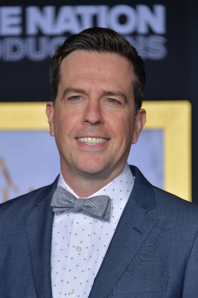 Ed Helms in blue suit and gray bow tie at formal event with blurred background wallpaper