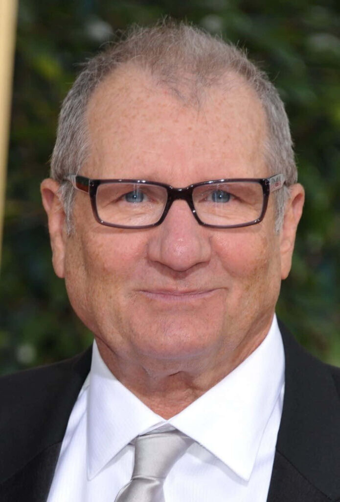 Ed ONeill close-up portrait with black-rimmed glasses smiling against blurred green background wallpaper