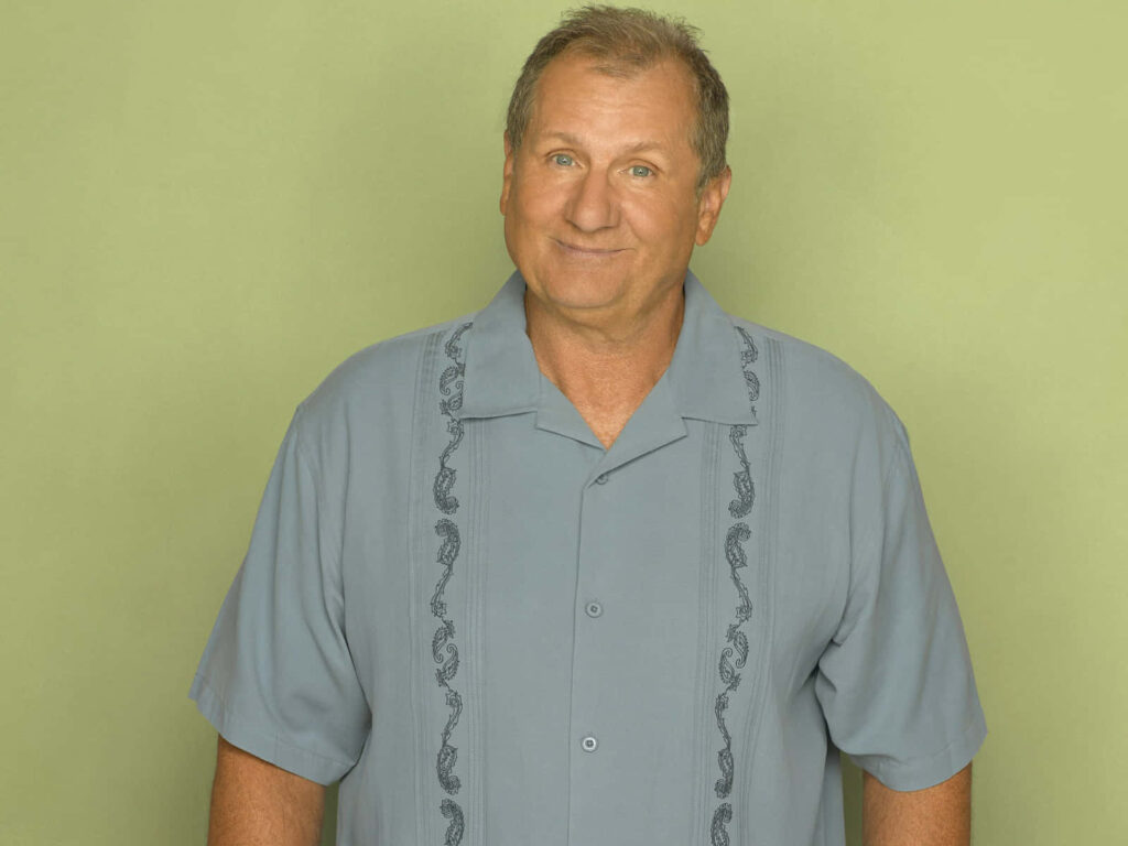 Ed O'Neill in light blue patterned shirt against soft green wallpaper background portrait