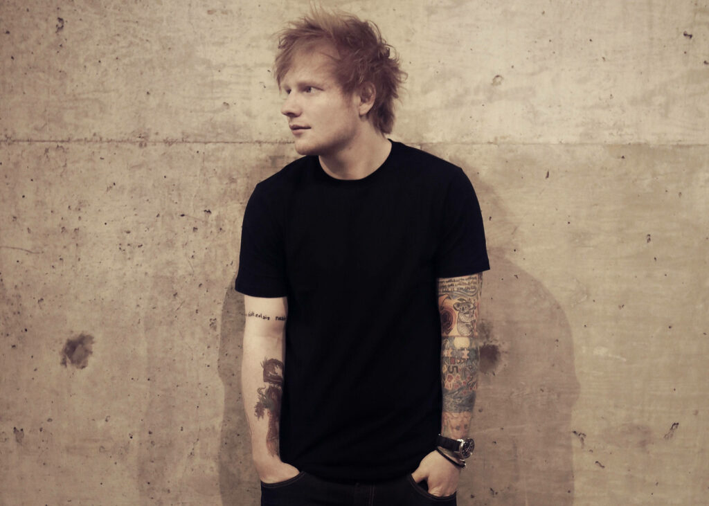 Ed Sheeran Against Rustic Wall: Artistic Tattooed Wallpaper Background