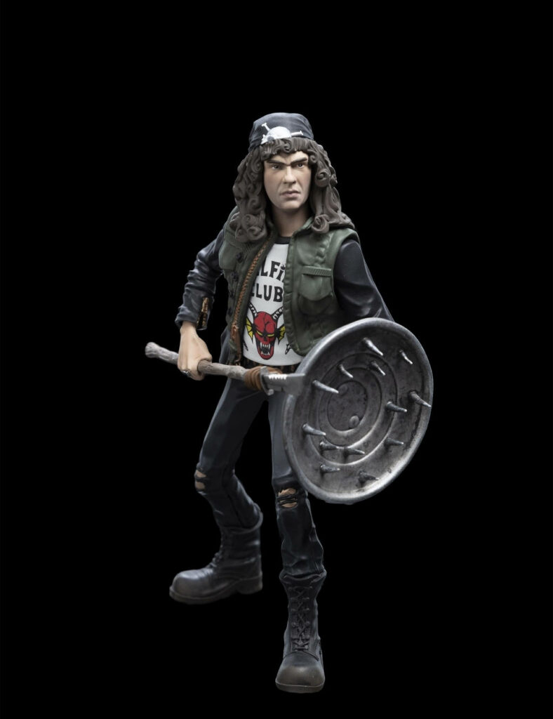 Eddie Munson in Hellfire Club shirt grips shield device with intense dark textured wallpaper background