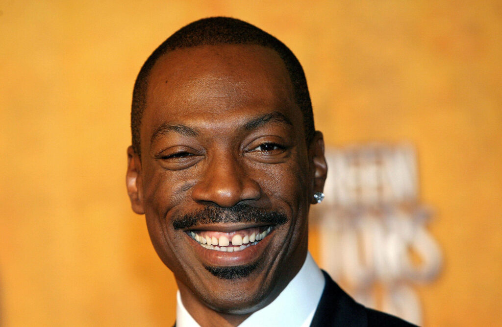 Close-up of Eddie Murphy smiling with tooth gap on vibrant golden background wallpaper