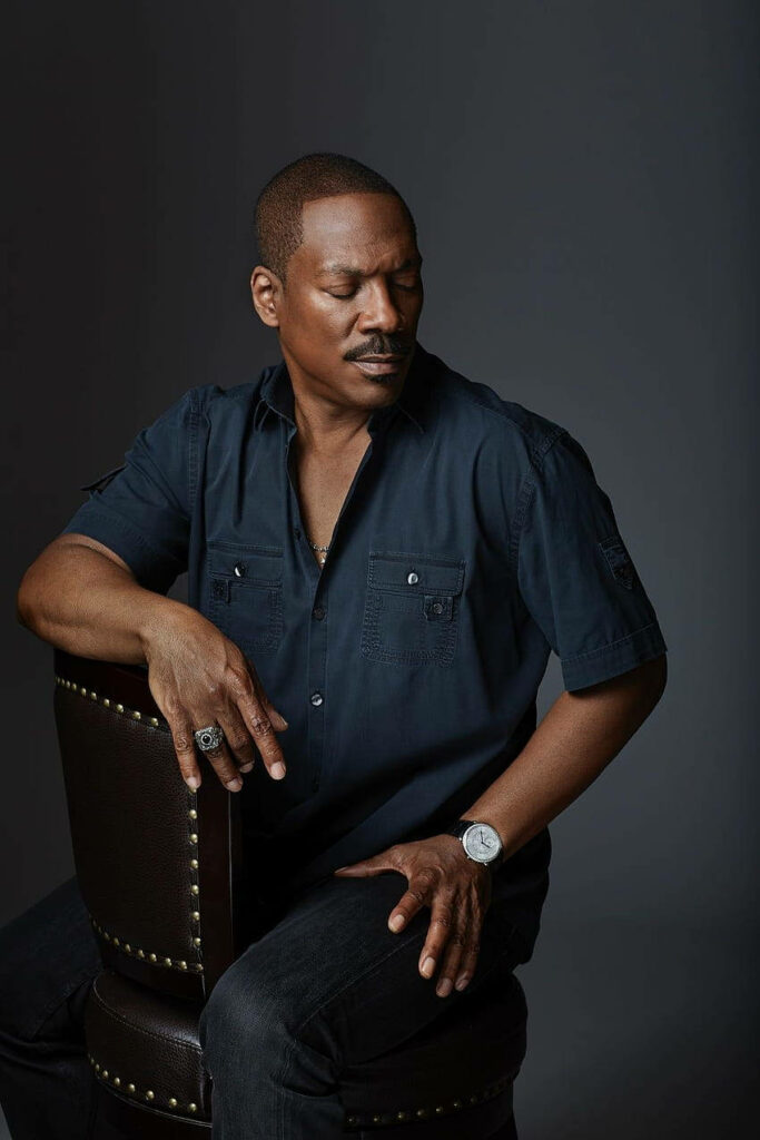 Eddie Murphy studio portrait with dramatic lighting navy shirt silver accessories minimalist background Wallpaper