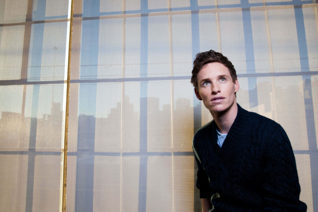 Oscar-winning Eddie Redmayne in dark sweater with geometric window and cityscape background wallpaper