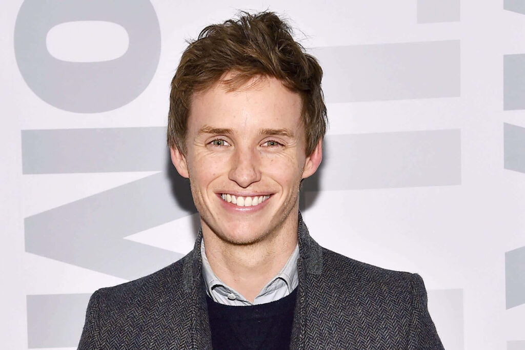 Eddie Redmayne smiling in tweed blazer and light blue shirt against soft gray background wallpaper