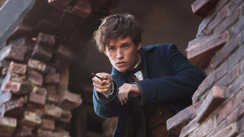 Eddie Redmayne as Newt Scamander aiming wand through cracked brick window magical adventure background Wallpaper