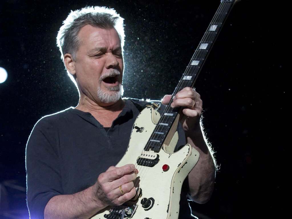 Eddie Van Halen passionately playing iconic guitar on stage with dramatic rock concert lighting background Wallpaper