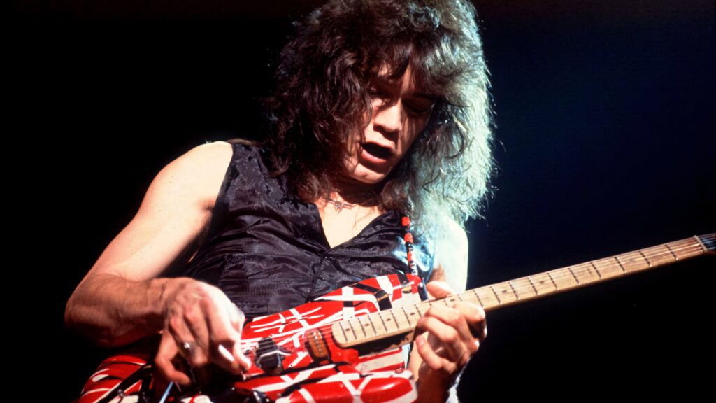 Eddie Van Halen playing iconic red white black striped guitar on stage with dynamic lighting Wallpaper