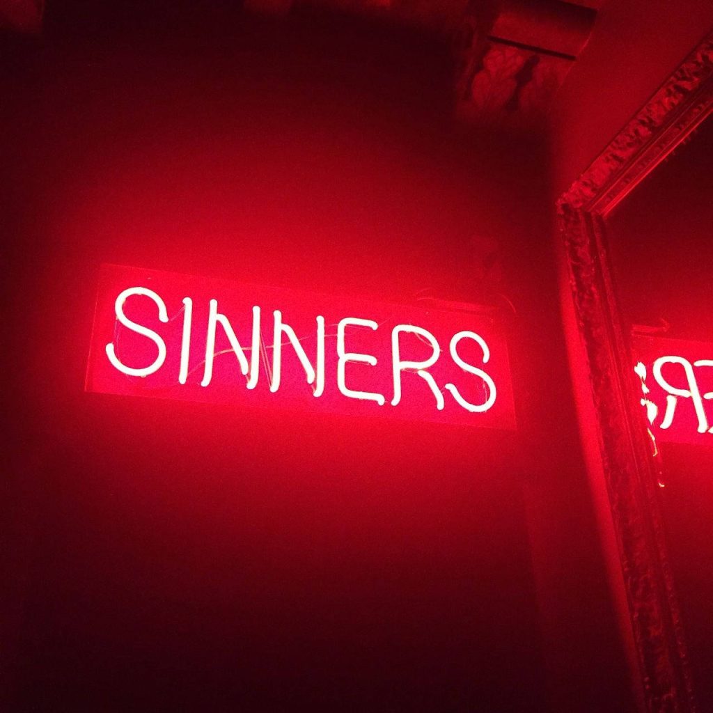 Edgy red neon SINNERS sign wallpaper with moody glow and mirror reflection dark background