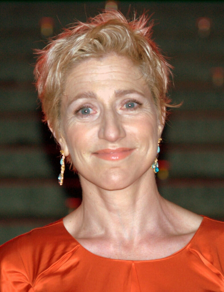 Edie Falco in orange outfit with short blonde hair soft background warm gentle expression wallpaper