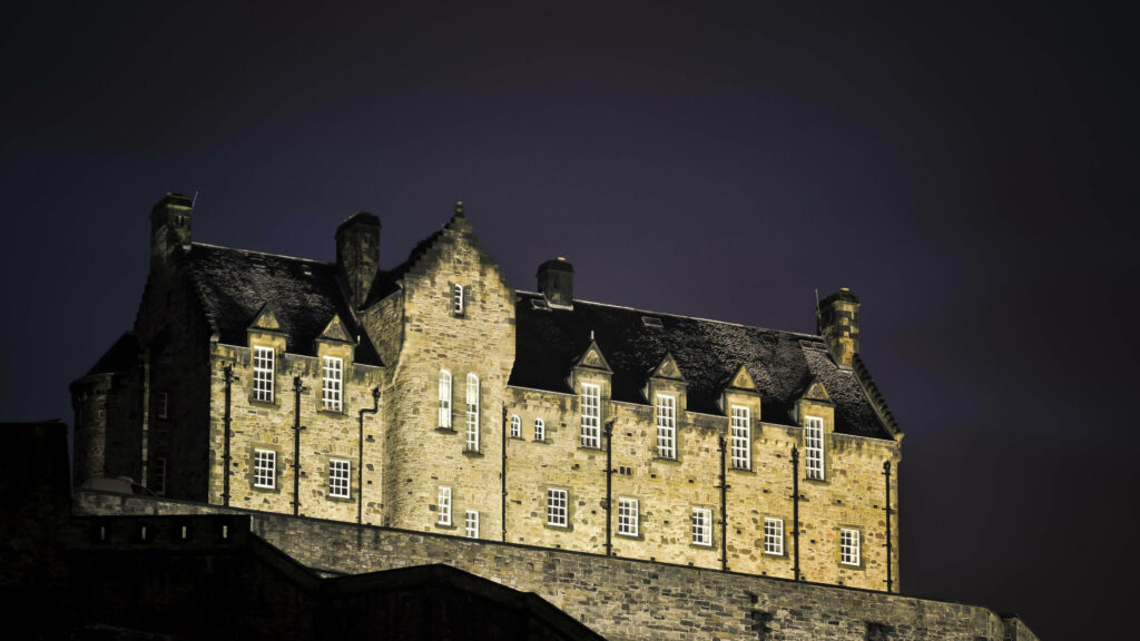 Edinburgh Castle illuminated at night with golden lights against a deep dark sky wallpaper background