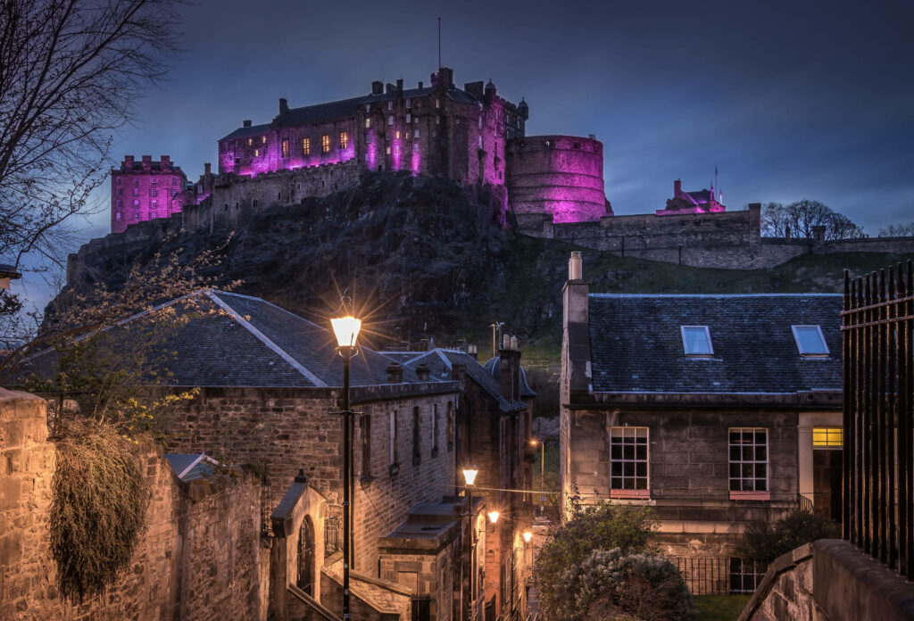 Edinburgh Castle illuminated in purple lights at dusk over historic cityscape wallpaper background