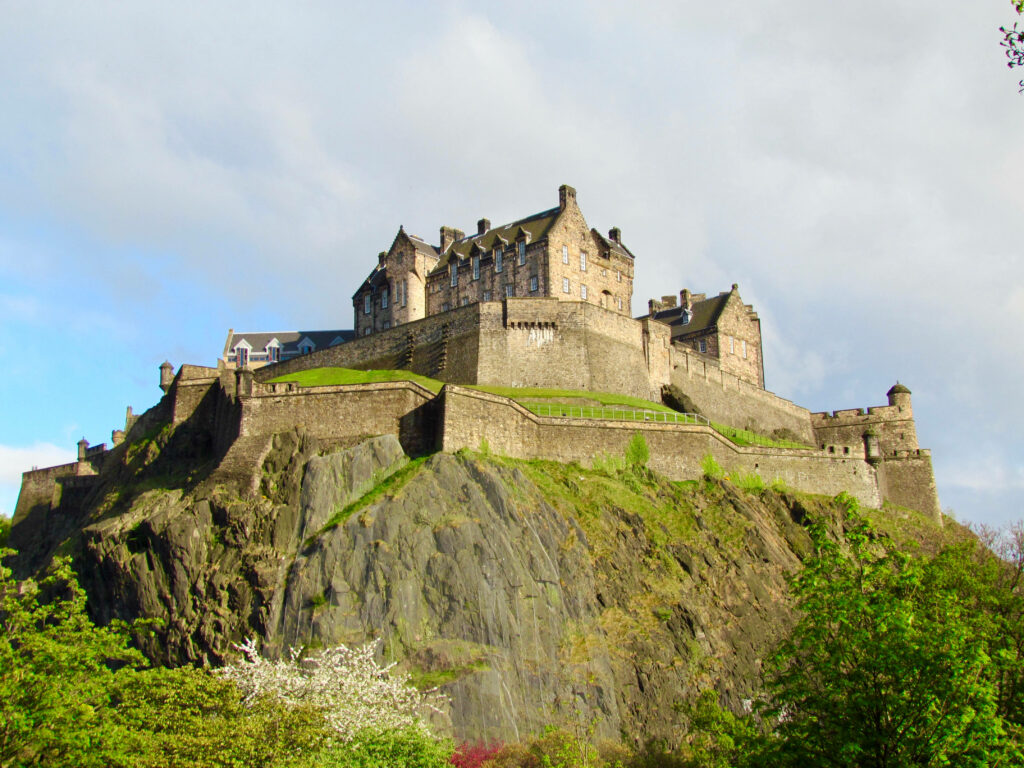 Edinburgh Castle on rocky hill with lush greenery and warm sunlight historic stone architecture Wallpaper