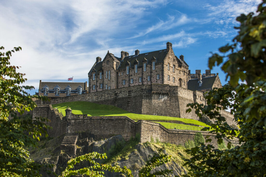Edinburgh Castle on rocky hill with lush greenery under blue sky historic Scottish landmark wallpaper