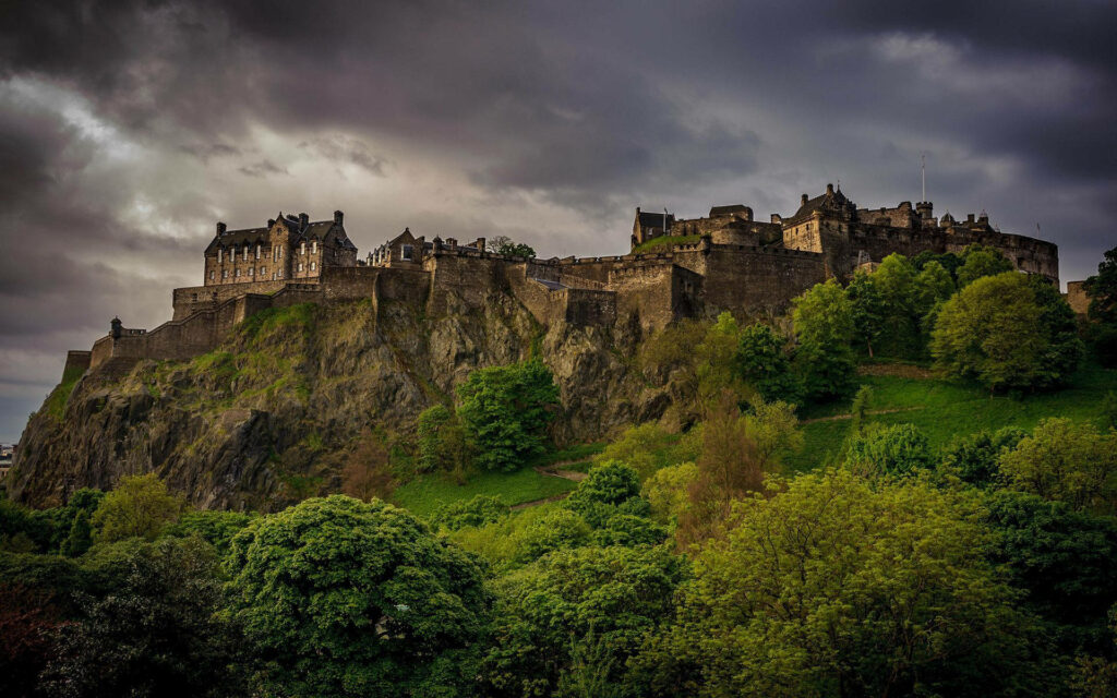 Edinburgh Castle on rugged hill with lush trees under stormy dark clouds historic fortress view Wallpaper
