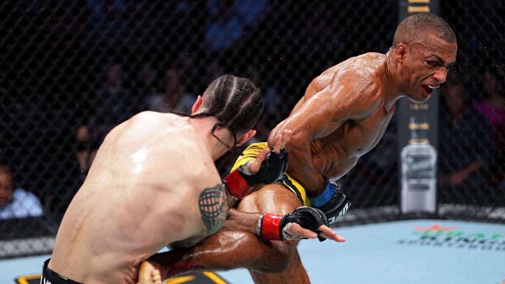 Edson Barboza landing a powerful knee strike in intense MMA fight inside octagon cage background Wallpaper