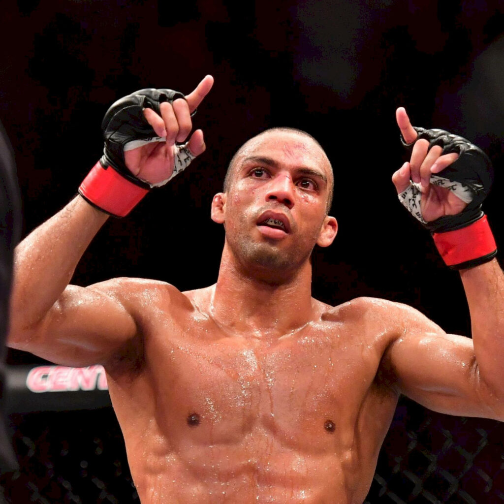 Edson Barboza celebrates victory in MMA ring with raised fists and muscular sweat-soaked physique Wallpaper