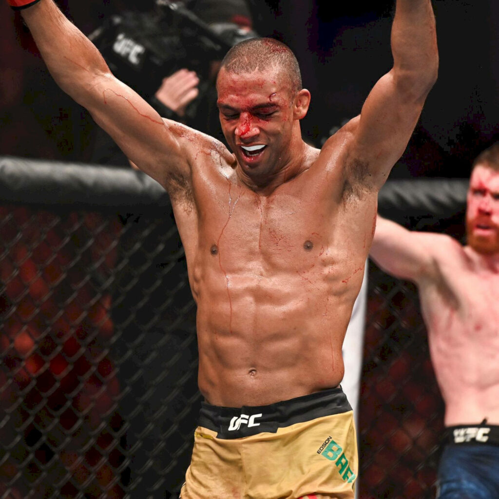 Edson Barboza triumphs in UFC octagon with arms raised and a bloody nose under bright lights Wallpaper