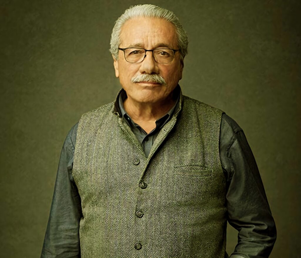 Edward James Olmos portrait in herringbone vest on olive green textured wallpaper background